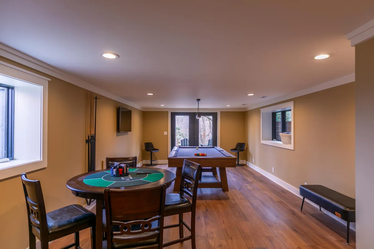 A vibrant game room featuring both a pool table and a poker table, illuminated by natural light from generous windows. The space exudes a lively, fun atmosphere, inviting guests to enjoy friendly competitions and memorable gatherings.