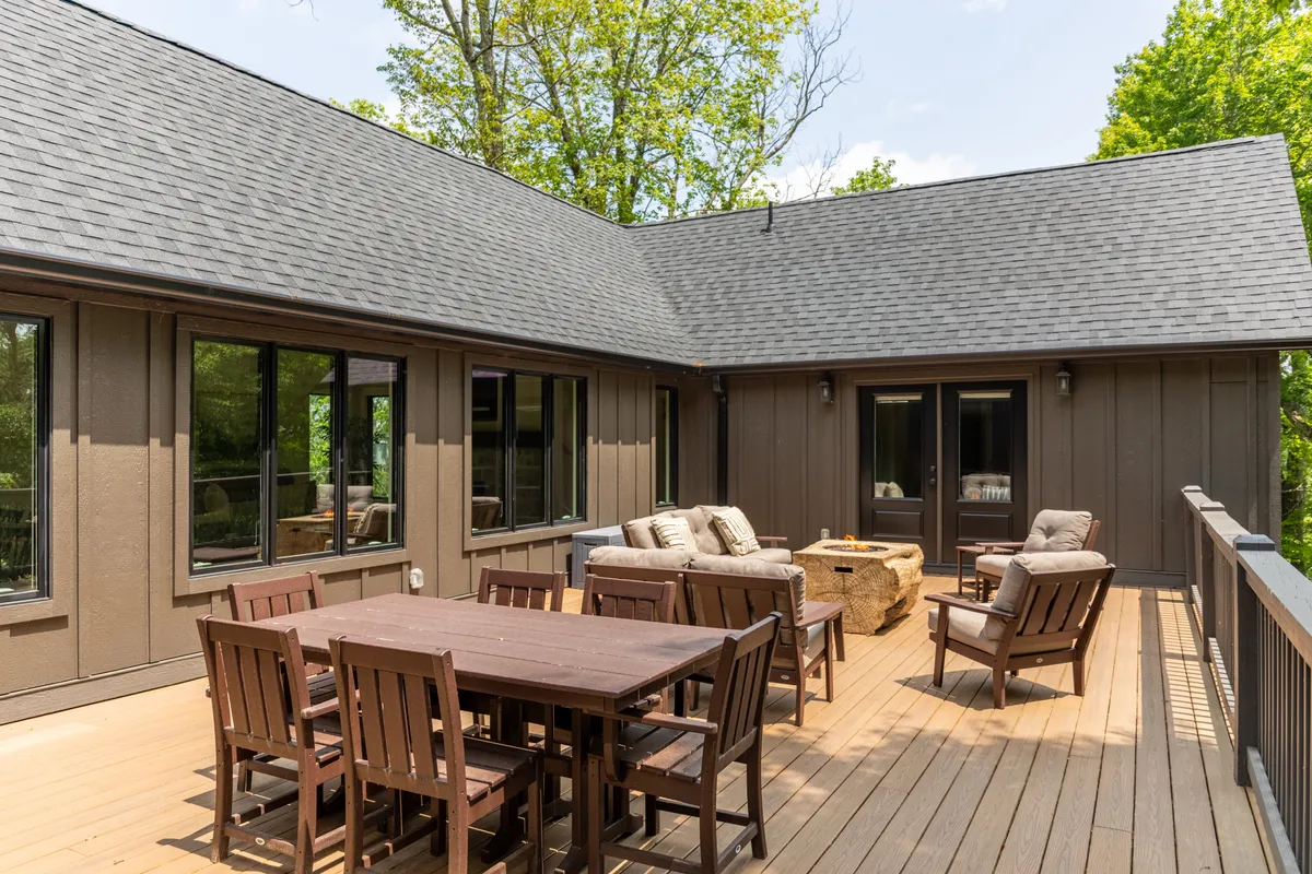 A spacious wooden deck features a dining table and comfortable sitting area nestled amongst tall trees, offering a serene spot for outdoor gatherings and immersion in nature.