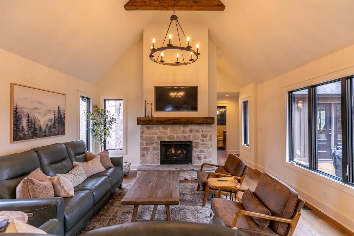 A welcoming living area featuring a cozy fireplace as its focal point, complemented by a plush sofa, coffee table, and elegant chandelier. The warm atmosphere suggests a perfect spot to unwind after outdoor adventures in any season.
