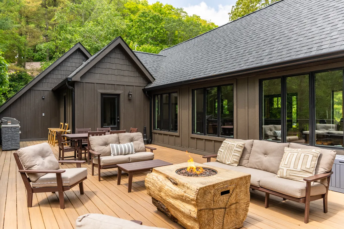 The image showcases the inviting exterior of the property, featuring a spacious wooden deck overlooking the serene Boone landscape. A cozy fire pit is surrounded by comfortable outdoor seating, perfect for gathering with friends and family. The scene exudes a relaxed, welcoming vibe, ideal for enjoying sunsets, roasting s'mores, and making lasting memories together.