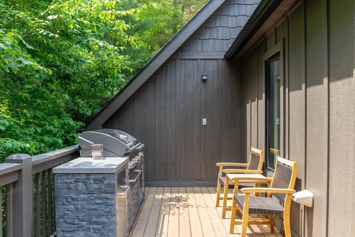 A wooden deck with a grill and comfortable chairs overlooks a natural landscape. The space encourages socializing—ideal for sunset barbecues, morning coffee, or relaxed conversations under the stars, echoing communal enjoyment.