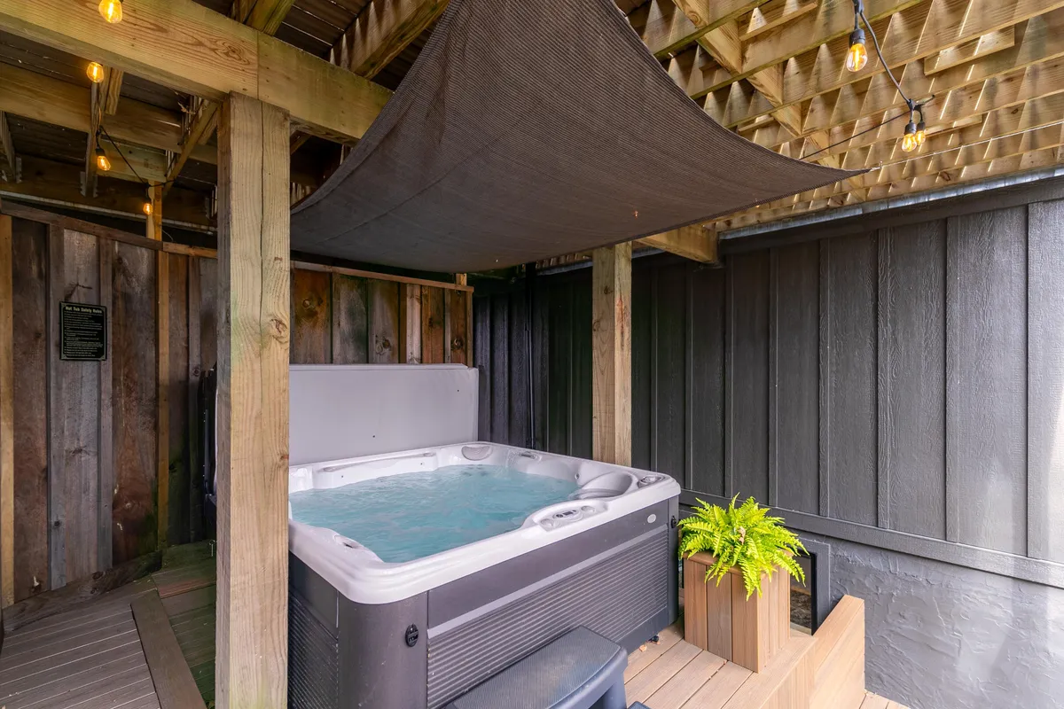 A luxurious indoor hot tub area with exposed wooden beams, ambient hanging lights, and lush potted plants, exuding a tranquil, spa-like atmosphere perfect for year-round relaxation and socializing.