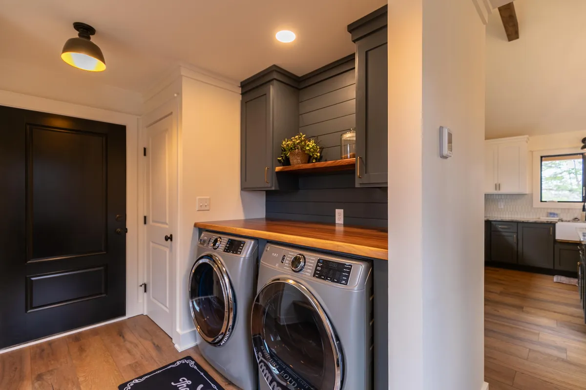 This image shows a functional laundry area with a modern washer and dryer, wood countertop for folding, and dark cabinetry for storage. The space is tidy and practical, emphasizing ease and convenience for families on the go.