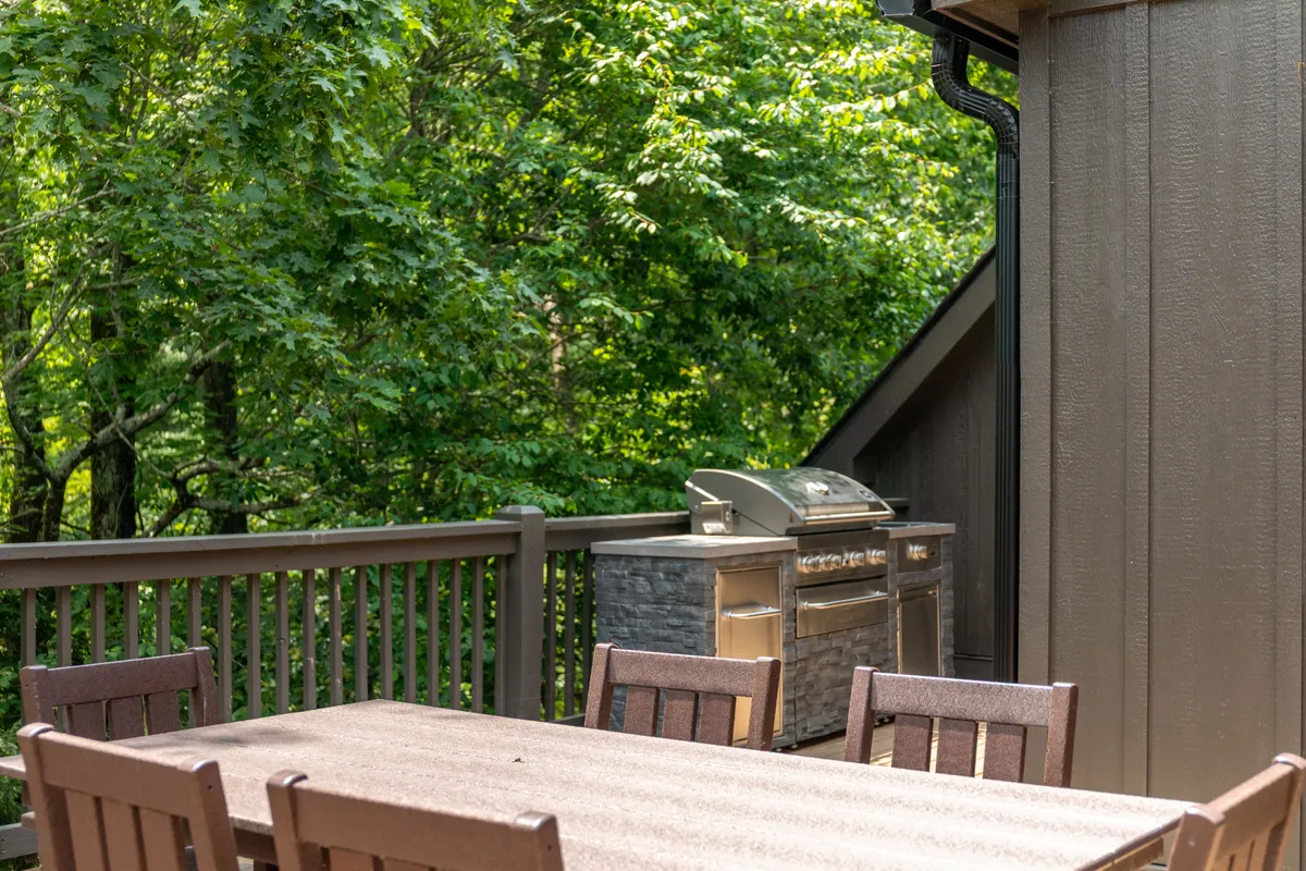 An outdoor dining area with a table and grill, surrounded by greenery. This space invites outdoor dining, barbecues, or simply enjoying nature with loved ones—including four-legged family members.