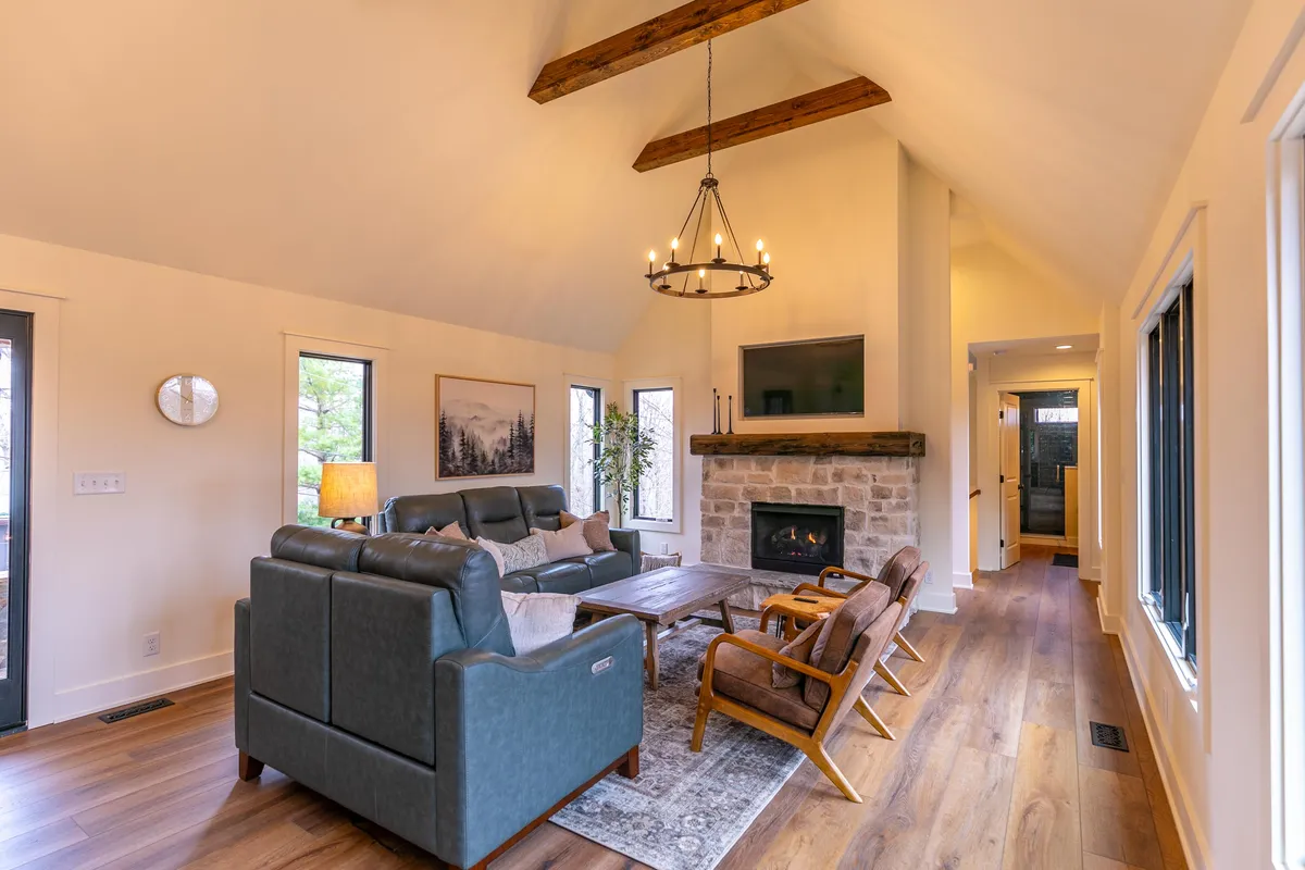 A spacious living room with a stone fireplace as the centerpiece, comfortable seating, large windows revealing scenic views, and a statement chandelier—an inviting common area perfect for family gatherings.