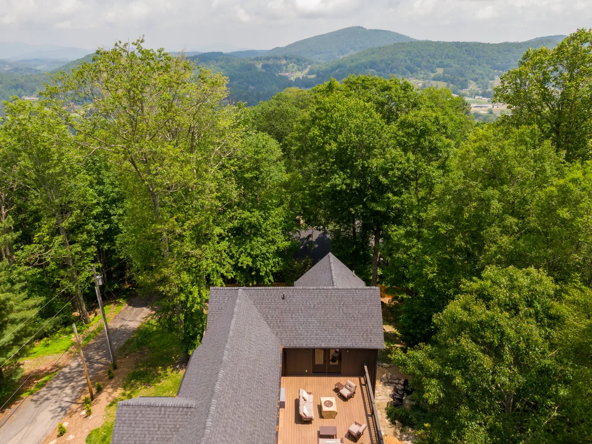 A broad view of the home’s exterior, showing the expansive wooden deck surrounded by mature trees and distant mountain scenery. The inviting deck features outdoor seating that suggests a relaxing spot to unwind after a day out exploring Boone.